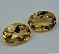 Close-up view of two oval faceted citrine gemstones side by side showing their transparent yellow color and brilliance.