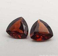 Pair of deep reddish-brown garnets cut in trilliant shape, showing facets and color.