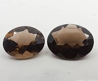 Top view of two oval smokey quartz gemstones showing faceted surface and varying brown color intensity.