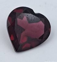 Close-up image of deep red heart-shaped garnet gemstone showing facets and surface condition.