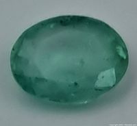 Close-up front view of the oval-shaped emerald gemstone showing internal inclusions and overall bluish-green color.