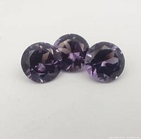 Photo showing three round faceted amethyst gemstones together, displaying their purple shades and faceting.