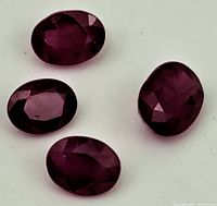 Four oval faceted natural rubies displayed on a white background, showing the color and cut for all stones.