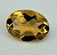 Close-up front view of yellow-golden oval faceted citrine gemstone showing faceting and color.