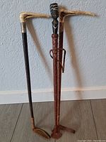 Three African vintage riding crops displayed leaning against a wall showing overall condition and unique carved handles