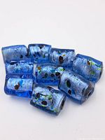 Group of ten blue glass beads showing their shapes, embedded colorful spots, and translucent blue surfaces with internal bubbles.