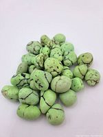 Pile of multiple small to medium oval green beads with black veining on white background