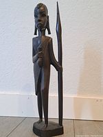 Front view of dark hardwood statue of an African woman holding a spear, standing on an oval base.