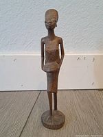 Front view of the wooden African woman statue standing holding a bowl, displaying detailed facial carving and the figure's posture.