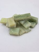 View of a pile of rectangular jade bead blocks showing varying shades of green and smooth surfaces.
