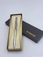 Silver-tone Parker pen displayed inside original box with cream-colored liner, showing textured body and clip.