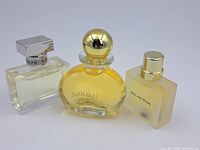 Three miniature perfume bottles on a plain surface in used condition, details visible showing brand names and bottle shapes.