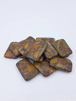 Group of polished rectangular picture jasper beads with natural patterns in earth tones arranged loosely together.