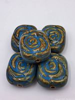 Five porcelain rose beads stacked, showing front embossed design in blue and brown with gold highlights.