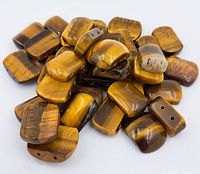 Multiple polished Tigers Eye rectangular beads in assorted sizes scattered to show their shape, color, and drilling for stringing.