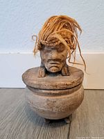 Front view of the wooded Tiki container with rope hair on the lid.