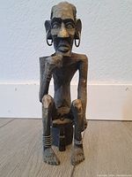 Front view of the wooden African man statue showing facial features and seated posture.