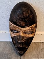 Front view of the wooden African mask showing the dark brown face, carved features, and tan eye band