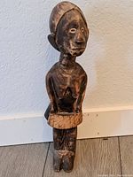 Front view of the wooden African woman statue showcasing the carved face, torso, and skirt details.