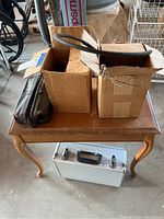 Overview of items on wooden table including cardboard boxes, leather shaving kit bag and white metal case on the floor.