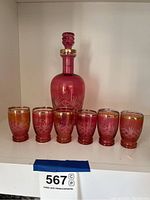 Front view of cranberry glass decanter with six matching small cups showing gold rim and etched details.