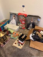 Assorted boxed and loose dolls, including Bridal Barbie, Coca-Cola Barbie, and Snow White Disney doll, along with other collectibles and miscellaneous items on carpet.