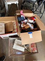 Large open cardboard box filled with various Beanie Babies and larger stuffed animals along with adjacent boxes/containers.
