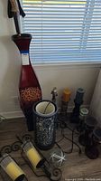 Photo showing tall red and black lamp base, blue and white ceramic candle holder, several candles on various holders, and a damaged cane/walking stick holder.