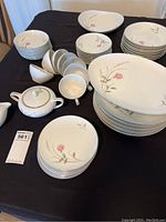 Full view of the china set including plates, bowls, cups, and covered sugar bowl or teapot, all decorated with a rose floral pattern.