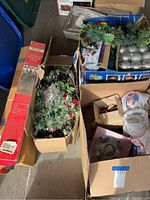 View of multiple boxes containing artificial Christmas trees and assorted Christmas ornaments including silver balls and garlands