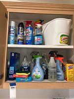 Photo of upper cabinet shelf showing various spray bottles and a white plastic bucket with Libman label.