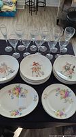 Full set of 9 Christmas-themed hand-painted Lennox plates with 22K gold detailing alongside 11 clear crystal goblets of varying sizes, and 3 floral design plates with minor chip visible on one plate