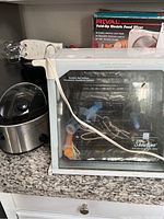 Photo showing Showtime Rotisserie Oven with accessories inside and Rival Fold-Up Electric Food Slicer boxed behind it on countertop.