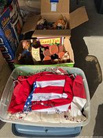 Box containing Halloween and Fall themed decor with small scarecrow dolls and pumpkin figures.