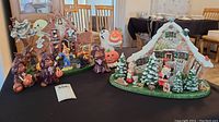 Photo showing two hand painted ceramic holiday village sets on a table, the Halloween set on the left and the Christmas set on the right.
