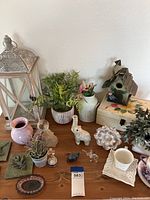 Overview of home decor items on wooden surface including fake plants, elephant figurines, vases, birdhouse, glass figurines, and candle holder