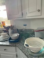 Kitchen counter with Pyrex glass bakeware, ceramic bowls, colander, and other kitchen items.