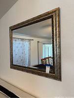 Front view of large rectangular mirror with textured silver frame hanging on a wall above a piece of furniture.