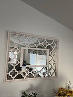 Front view of the square white shabby chic mirror showing the quatrefoil openwork frame and the central smaller rectangular mirror.