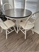 Full view of round dining table with dark top and four white chairs around it.