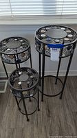 Three black metal side tables of varying heights and diameters with round mirrored tops and decorative jewels embedded around the edges, arranged grouped together
