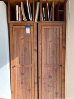 Front view of two tall wooden cabinets with vertical slat paneled doors and vintage file shelving on top containing folders.