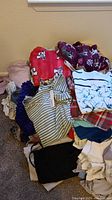 Pile of assorted women's clothing including fleece tops with animal prints, floral and plaid shirts, knitwear, and plain items