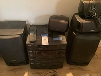 Wide front view of the Aiwa stereo system including the main stereo unit, speakers, and remote control on top.