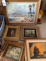 Group of five framed paintings showing coastal, figure, castle, landscape, and sunset scenes.