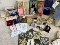 Overview photo showing three vintage Barbie dolls in original boxes including Winter Velvet and Spring Blossom Barbies, one boxed Annie Oakley doll, three vintage facial devices, multiple pieces of costume jewelry in cases, and a spread of vintage black and white movie star birthday cards.