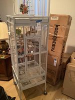 Front view of tall rectangular metal birdcage with stand and wheels, showing door with latch and interior wooden perches.