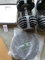 Two Bowflex adjustable dumbbells on stands with bubble-wrapped Chair Gym Twister exercise board and white mechanical bathroom scale visible