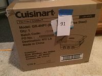 Photo of the box displaying the Cuisinart brand, model GR-4NP1, and details about the 5-in-1 griddler, made in China with destination NY/LA.