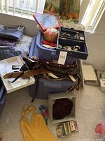 Overview of fashion belts, costume jewelry box, a decorative beaded bag, collectible plate, candle, and other miscellaneous items stacked near storage bins.